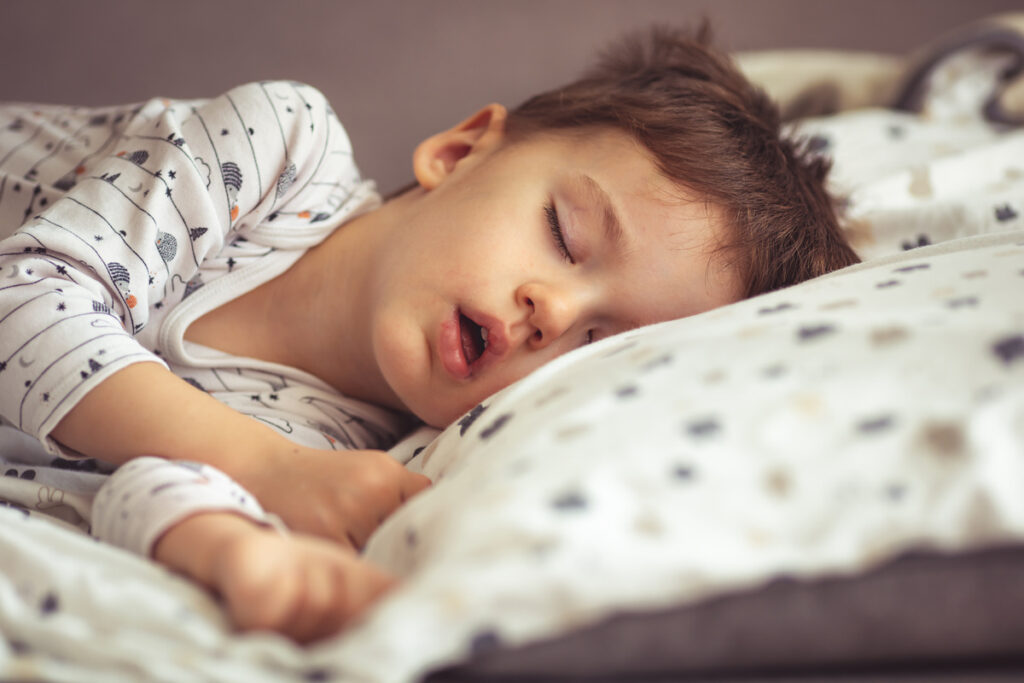 Little blond boy sleeping in his bed. Restless sleep of a baby w