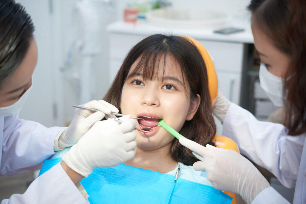 Professional female dentists examining oral cavity of young Asian girl in chair in office working in team